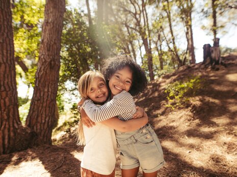 Zwei Kinder stehen im Wald und umarmen sich. 